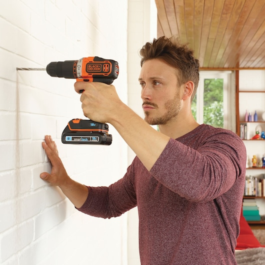 BLACKDECKER BDCHD18KBST cordless drill being used on a white brick wall in a home interior.