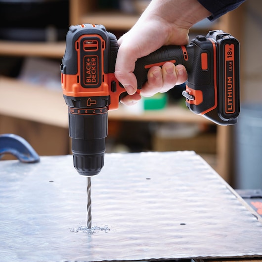 BLACKDECKER BDCHD18K cordless drill in use, orange and black, drilling into metal sheet.