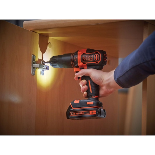 BLACKDECKER BDCHD18 cordless drill in use on cabinet hinge, with LED light, black and orange finish.