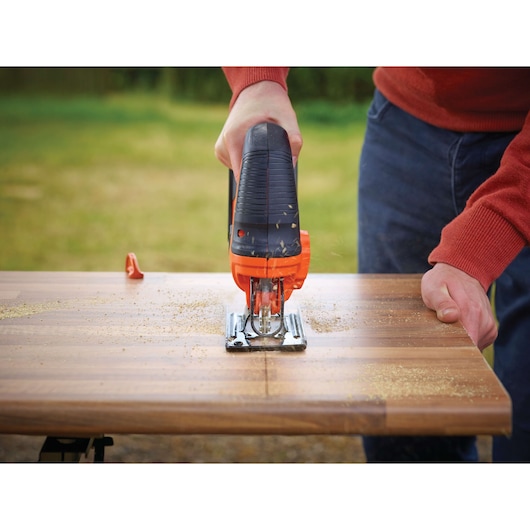 BLACK+DECKER BDCJS18 jigsaw in use cutting a wooden board outdoors.