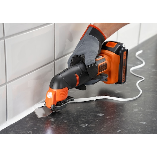 BLACKDECKER BDCOS18D1K cordless oscillating multi-tool being used to remove sealant from a kitchen countertop edge.