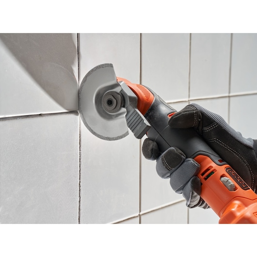 BLACKDECKER BDCOS18D1K multi-tool cutting white tile, close-up of tool in use.