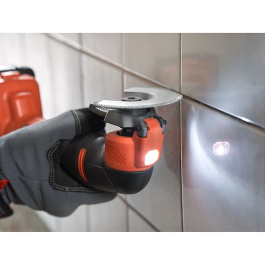 BLACKDECKER BDCOS18D1K cordless oscillating tool with LED light, close-up in use on wall tiles.