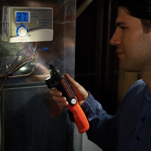 BLACK+DECKER BDCSFL20AT cordless screwdriver with orange and black handle being used near humidity control wires indoors.