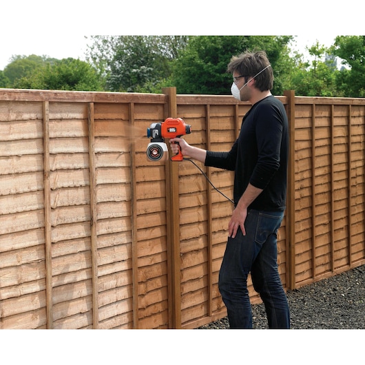 BLACKDECKER BDPS400 paint sprayer in use on wooden fence outdoors.