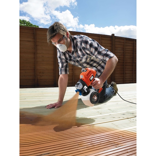 BLACKDECKER BDPS400 paint sprayer used outdoors on wooden decking, spraying brown paint, product in action.