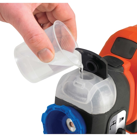Photo of BLACKDECKER BDPS400 paint sprayer with hand pouring liquid into transparent container, close-up, white background.