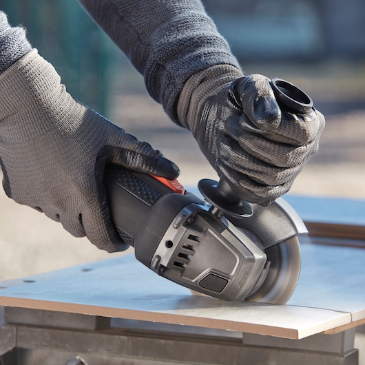 BLACKDECKER BEG220A6 angle grinder in use cutting a tile, close-up of gloved hands operating tool.