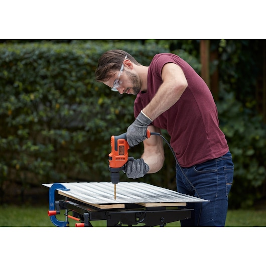 Person using a BLACK+DECKER BEH200K drill on a workbench outdoors, wearing gloves and safety glasses.