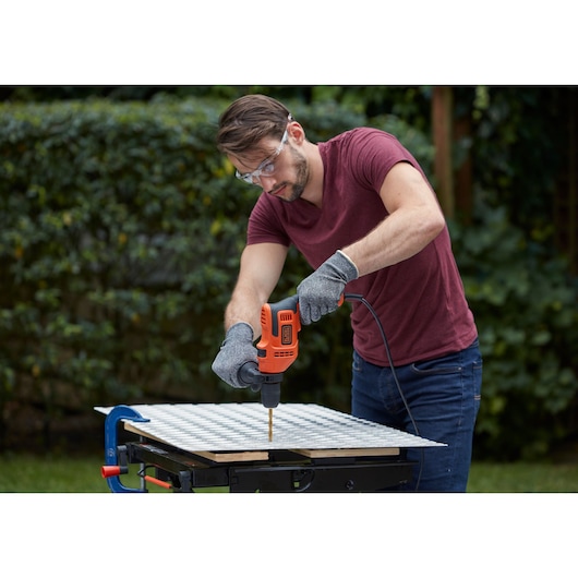 Person using BLACK+DECKER BEH200K drill with gloves outdoors on a workbench.