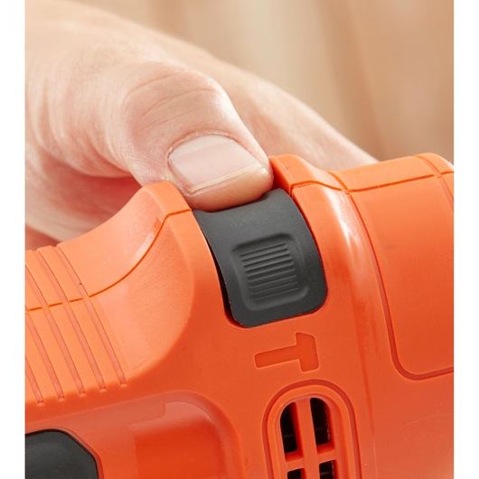 Close-up of a hand pressing a black button on an orange BLACK+DECKER tool.