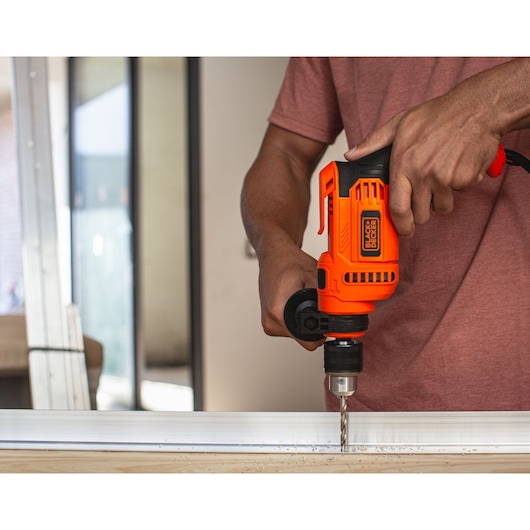 Photo of BLACK+DECKER BEH640 electric drill in use, drilling into metal, close-up of hands and tool.