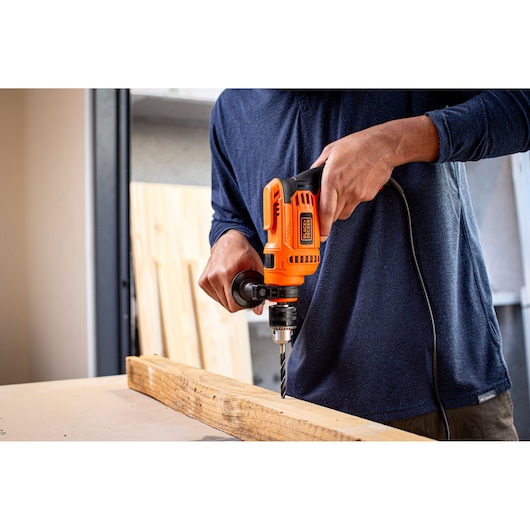 Person using BLACK+DECKER BEH640 corded hammer drill to drill into wood plank indoors.