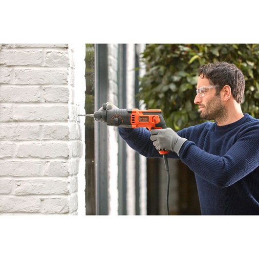 BLACKDECKER BEHS01 corded hammer drill in use on white brick wall, product photography.