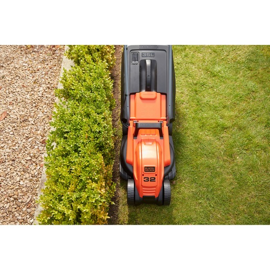 BLACK+DECKER BEMW451 lawn mower top view cutting grass along garden edge.