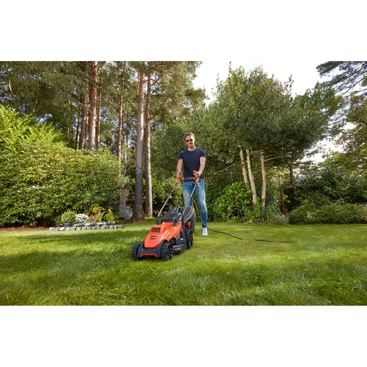 BLACKDECKER BEMW461BH lawn mower in use, orange body, user mowing grass in garden, outdoor scene.