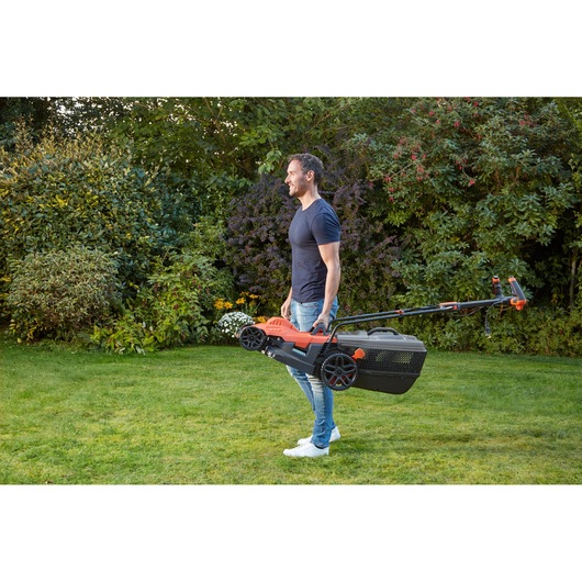 BLACKDECKER BEMW461ES lawn mower carried by person in garden, side view.