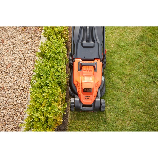 BLACKDECKER BEMW481BH electric lawn mower top view in use, orange and black design cutting grass near hedge.