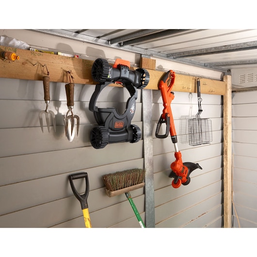 Photo of BLACK+DECKER BESTE630CM trimmer and mower parts hanging on a shed wall with other garden tools.