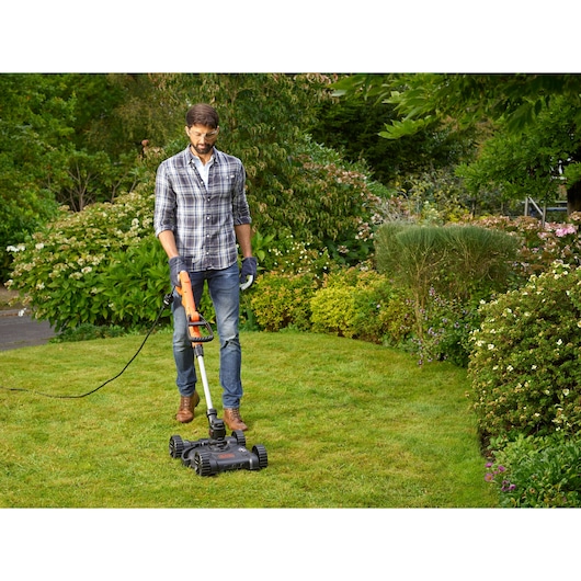 BLACKDECKER BESTE630CM lawn mower used outdoors on grass with garden background.