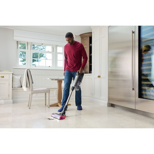BLACK+DECKER BHFEA640WG cordless stick vacuum cleaning kitchen floor near stainless refrigerator.