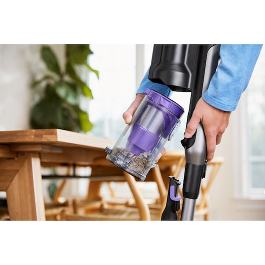 BLACKDECKER BHFEA640WP cordless vacuum being emptied, close-up on dust container with debris, wooden table in background.