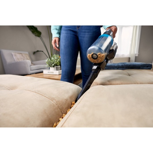 BLACKDECKER BHFEB520D1 handheld vacuum cleaning crumbs from beige sofa crevice in living room.