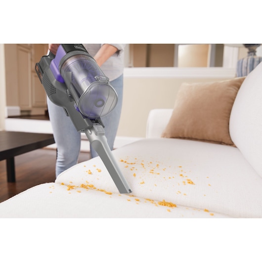 BLACKDECKER BHFEV182CP handheld vacuum cleaning crumbs from white sofa in living room.