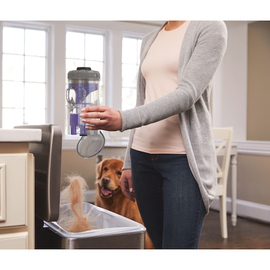 Photo of a person emptying pet hair from a BLACKDECKER BHFEV182CP vacuum canister into a kitchen trash bin.