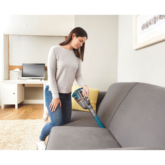 Photo of BLACKDECKER BHHV520BF handheld vacuum being used to clean a grey sofa in a modern living room.
