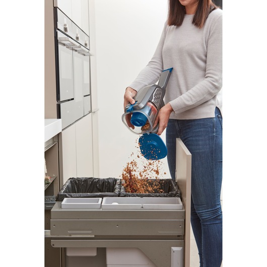 BLACK+DECKER BHHV520BF handheld vacuum being emptied into kitchen trash bin, showing open dust container.