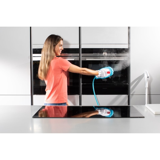 Photo of person using BLACKDECKER BHSM1615DSG handheld steam cleaner on oven door in modern kitchen.