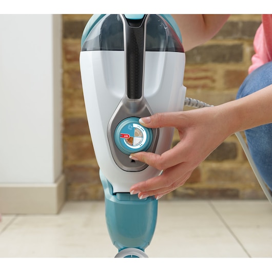 A close-up of a person adjusting the dial on a BLACK+DECKER steam mop, with the hand turning the control knob located on the front of the appliance.