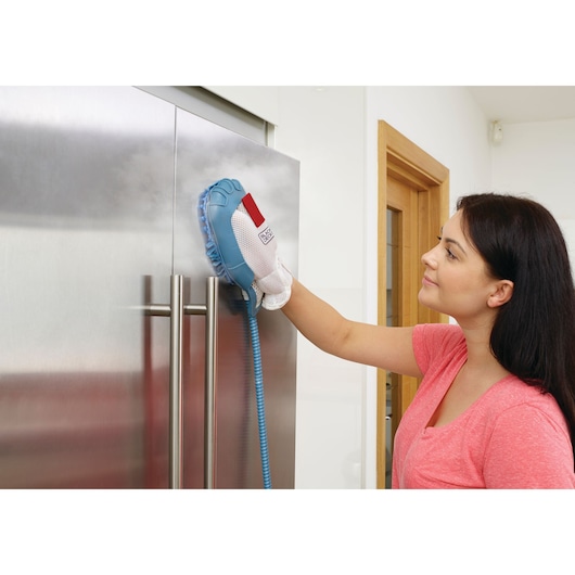 A person using a BLACK+DECKER steam cleaning glove to clean the surface of a stainless steel refrigerator door. The person's face is blurred for privacy.