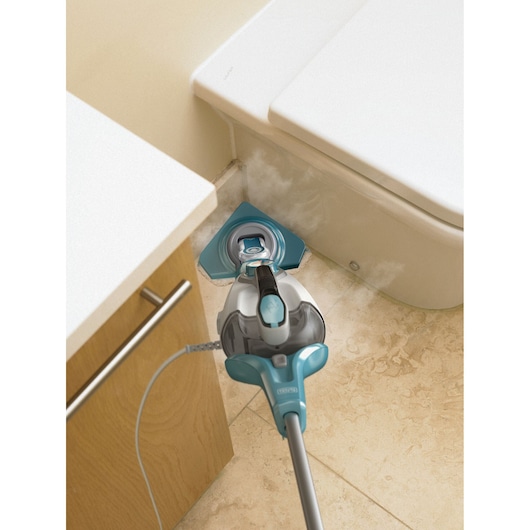 A BLACK+DECKER steam mop cleaning the tile floor in the corner between a bathroom cabinet and a toilet.