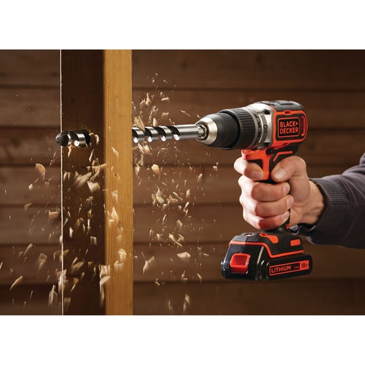 Photo of BLACK+DECKER BL188N cordless drill in use, drilling through wood with flying wood chips.