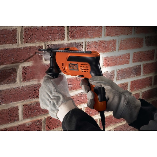 Photo of BLACKDECKER CD714CRES corded drill used on a brick wall by gloved hands.