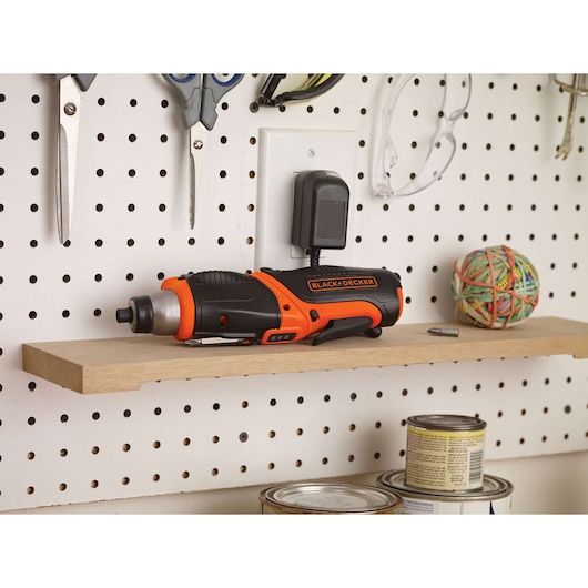Photo of BLACK+DECKER CS3653LC cordless screwdriver in black and orange, charging on a workshop shelf.