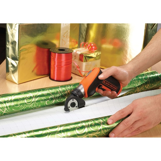 BLACKDECKER CSCA3 rotary cutter used to cut green patterned wrapping paper, gifts and ribbons in background.