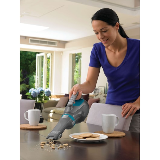 BLACKDECKER DV1210N handheld vacuum cleaning cookie crumbs from a dining table in a modern kitchen.