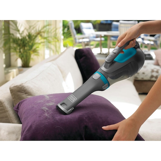 BLACKDECKER DV1210N handheld vacuum cleaning pet hair from a purple pillow on a sofa.