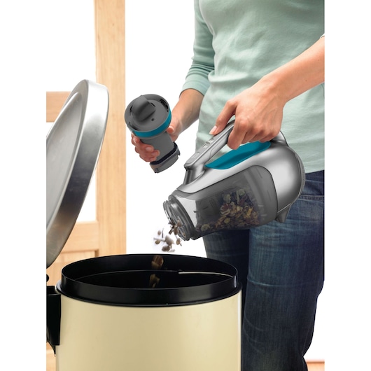 BLACKDECKER DV1210N handheld vacuum being emptied into a trash can, person holding filter.