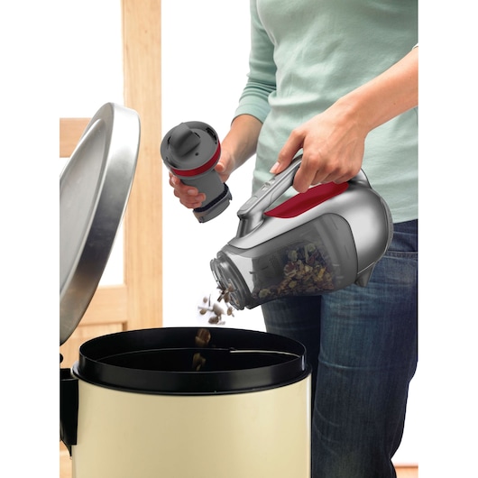 BLACKDECKER DV1415EL hand vacuum with debris being emptied into a trash bin, close-up photography.