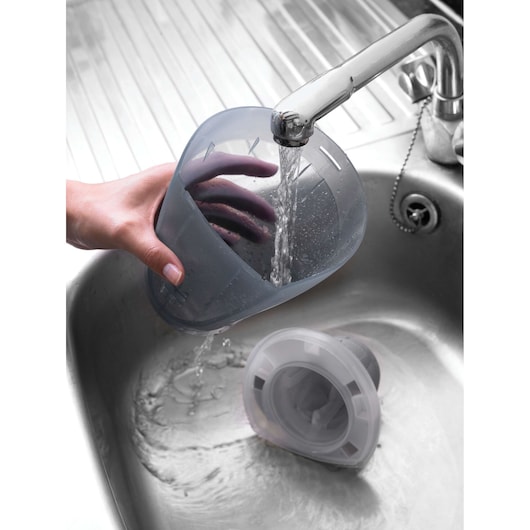 BLACKDECKER DV1415EL vacuum dust container being rinsed under tap water in a metal sink.