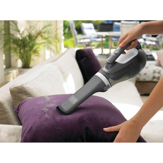 BLACKDECKER DV7215EL handheld vacuum cleaning pet hair from a purple cushion on a sofa.
