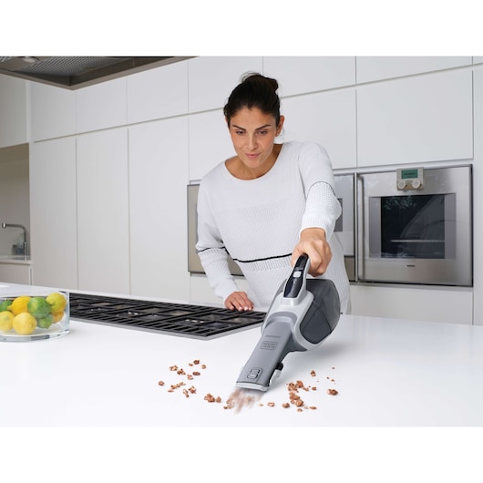 BLACKDECKER DVJ215J handheld vacuum cleaning crumbs on kitchen counter, woman in background.