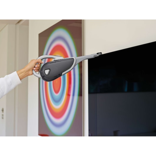 BLACKDECKER DVJ215J handheld vacuum cleaning TV screen in living room.