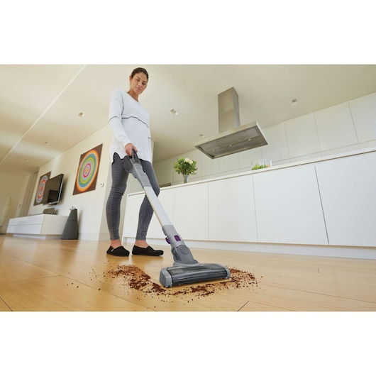 BLACKDECKER FEJ520JFS cordless stick vacuum cleaning debris on wooden floor in modern kitchen.