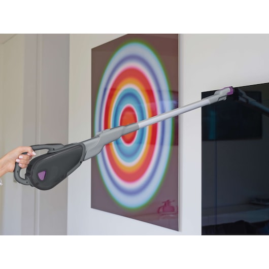 BLACKDECKER FEJ520JFS handheld vacuum with long extension cleaning a wall near colorful artwork.