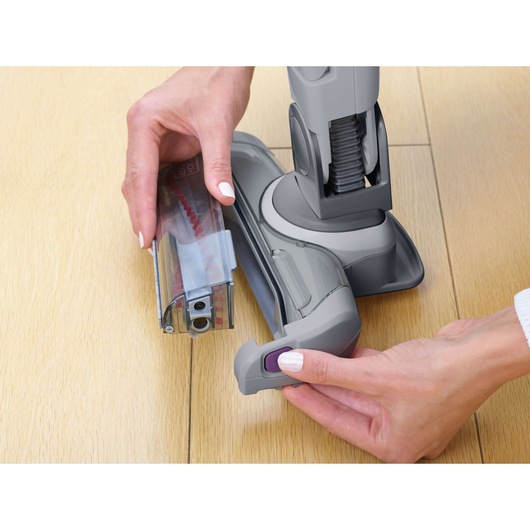 BLACKDECKER FEJ520JFS vacuum cleaner head close-up, hands removing brush roller attachment on wooden floor.